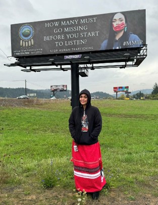 A photograph of Amanda Freeman standing beneath the billboard she designed.